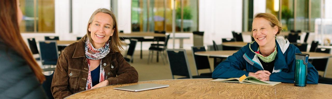 Teachers smile sitting outside at a table during Summer Institute